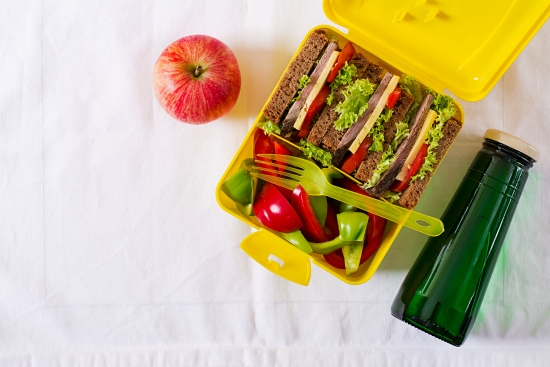 Healthy school lunch box with beef sandwich and fresh vegetables, bottle of water and fruits on white table. Top view. Flat lay